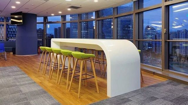 Inside the Beijing office, a white table with several stools stands next to a wall of floor-to-ceiling windows overlooking a city skyline.
